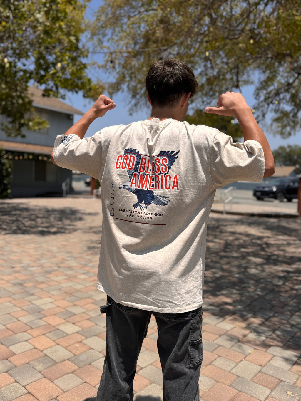 Person wearing a 'God Bless America' t-shirt outdoors on a sunny day.