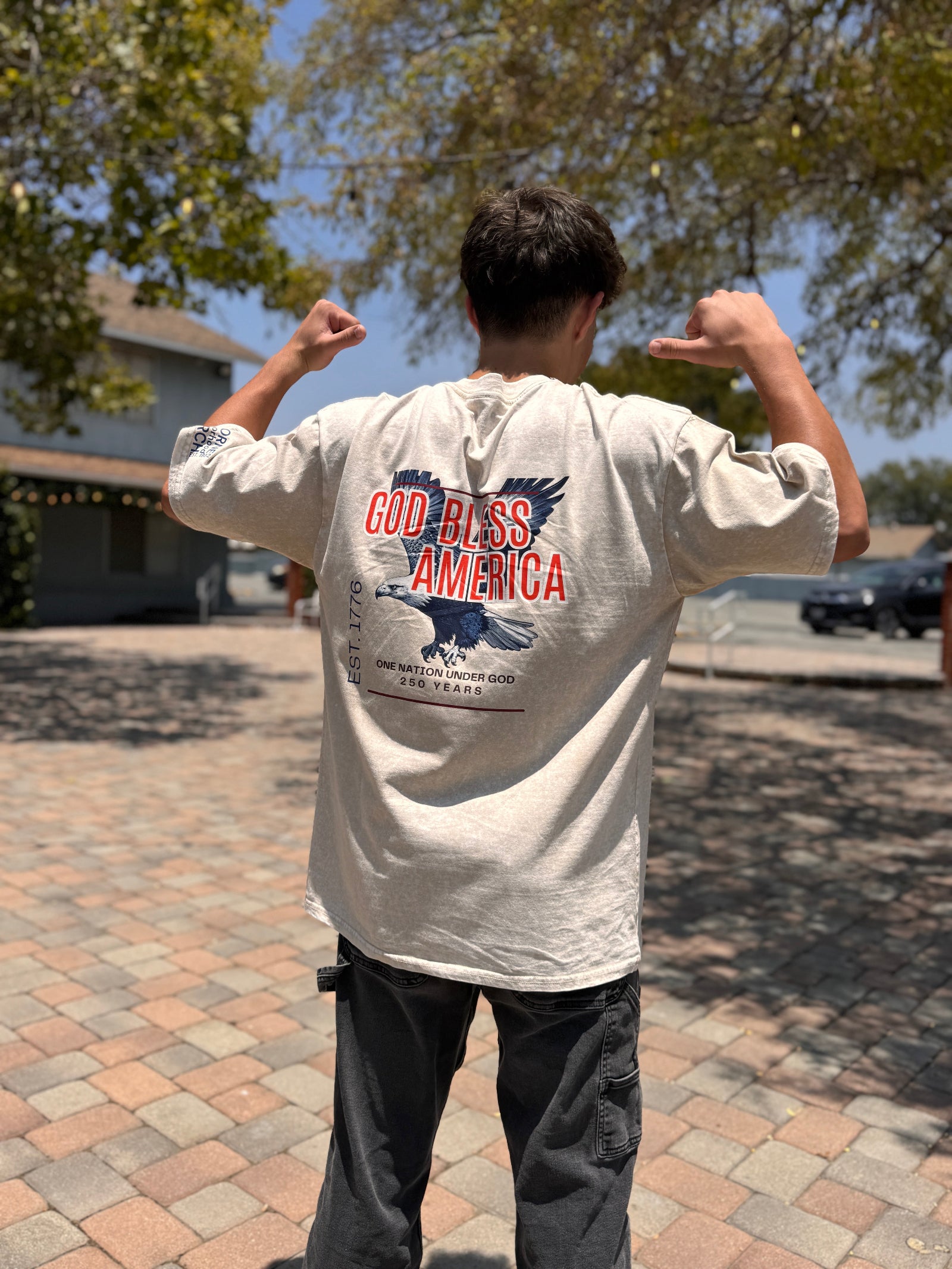 Person wearing a 'God Bless America' t-shirt outdoors on a sunny day.