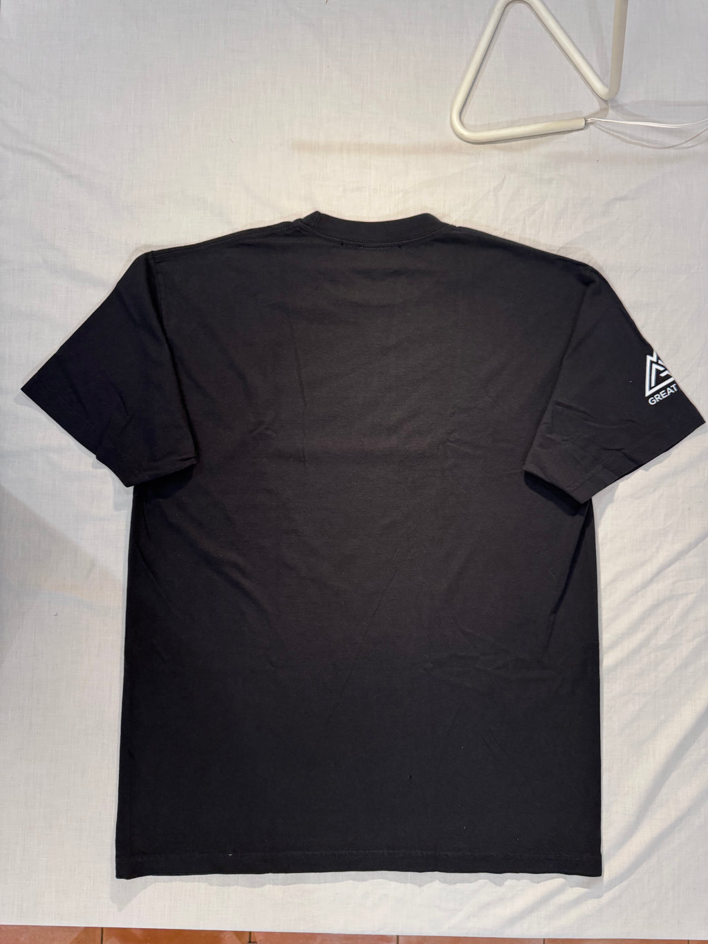 Black t-shirt with a logo on the back, hanging on a white hanger against a light background.