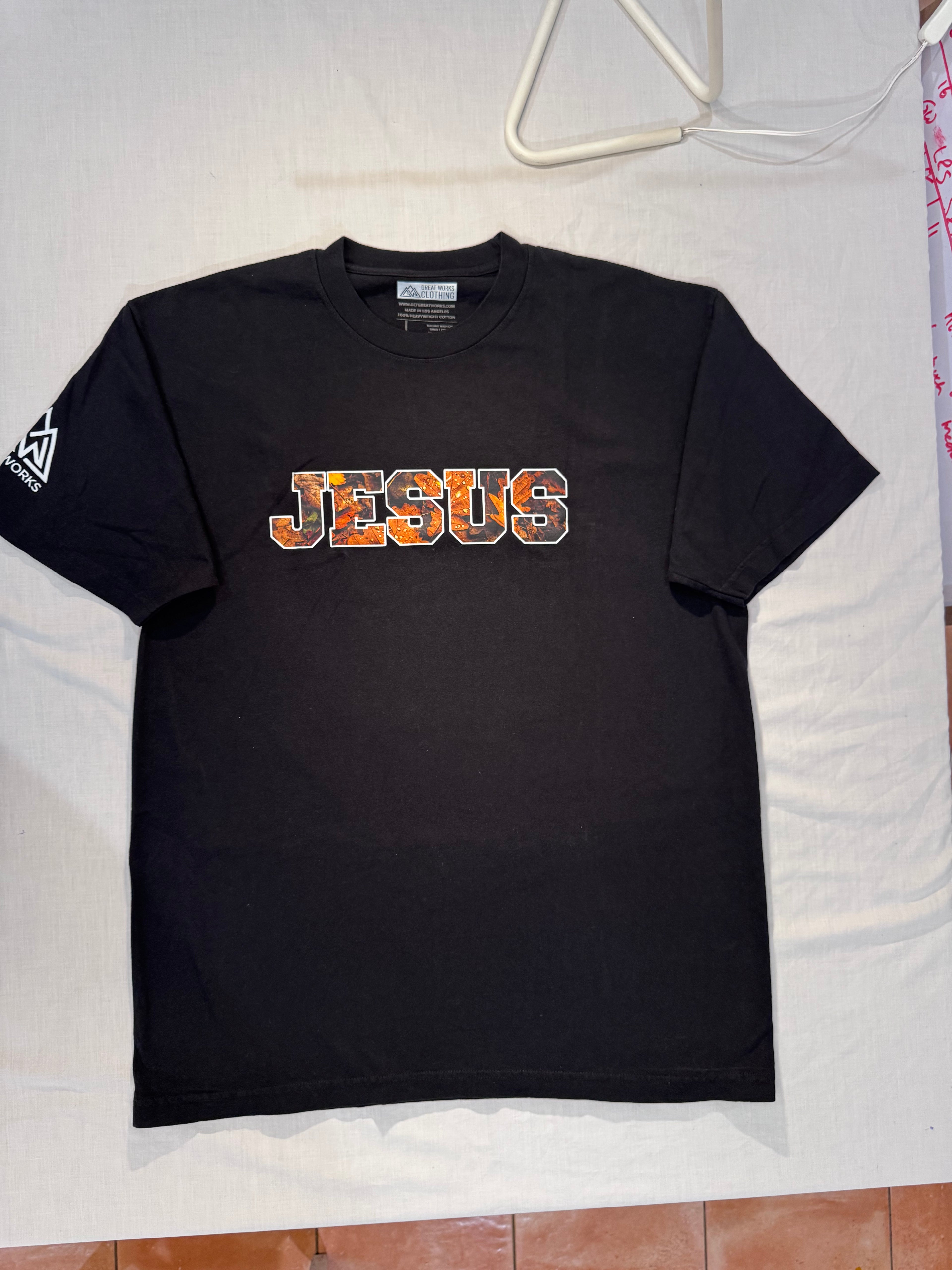 Black t-shirt with 'JESUS' printed on it, displayed on a white surface.