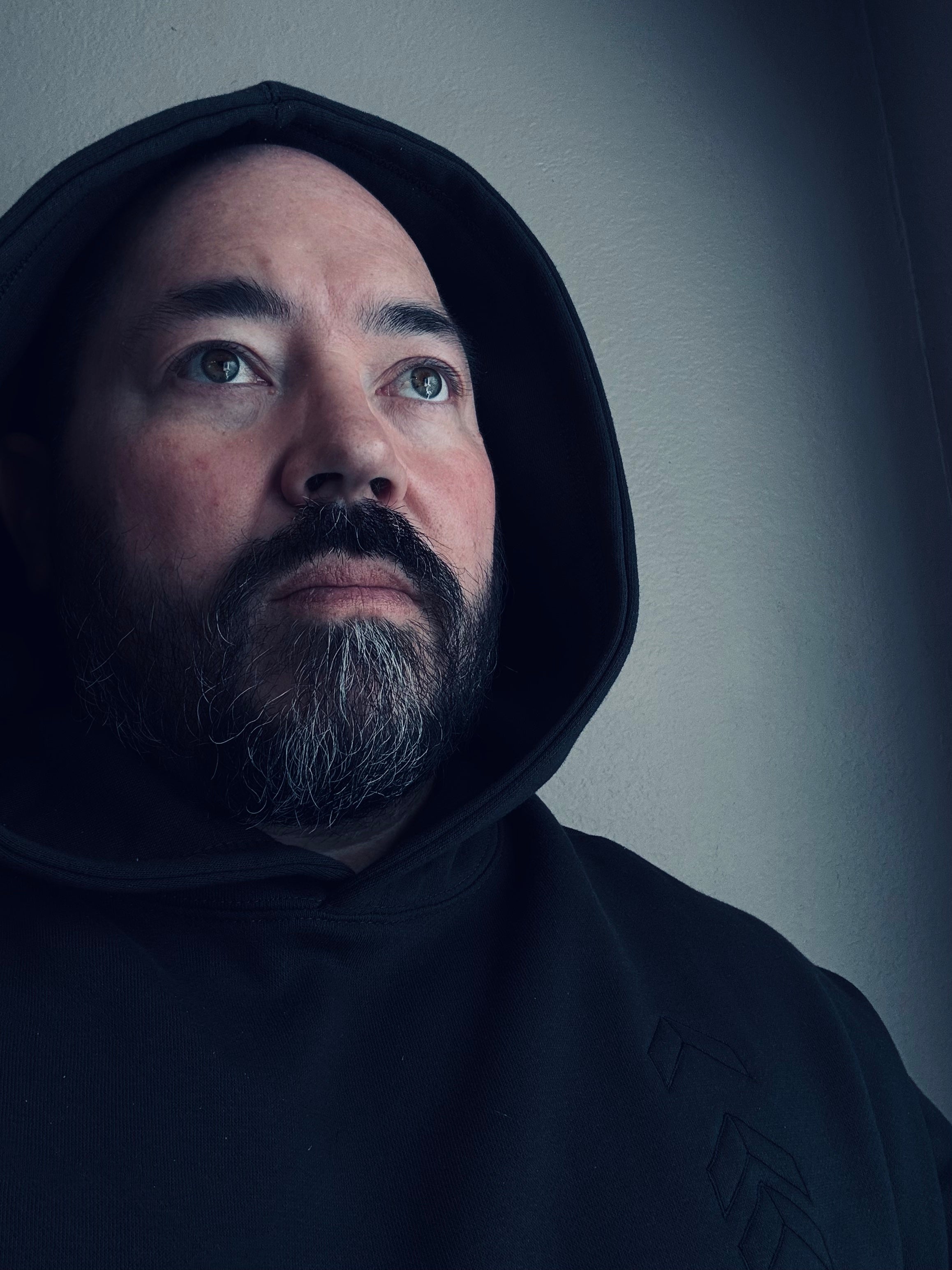 Man wearing a dark hooded garment against a plain background